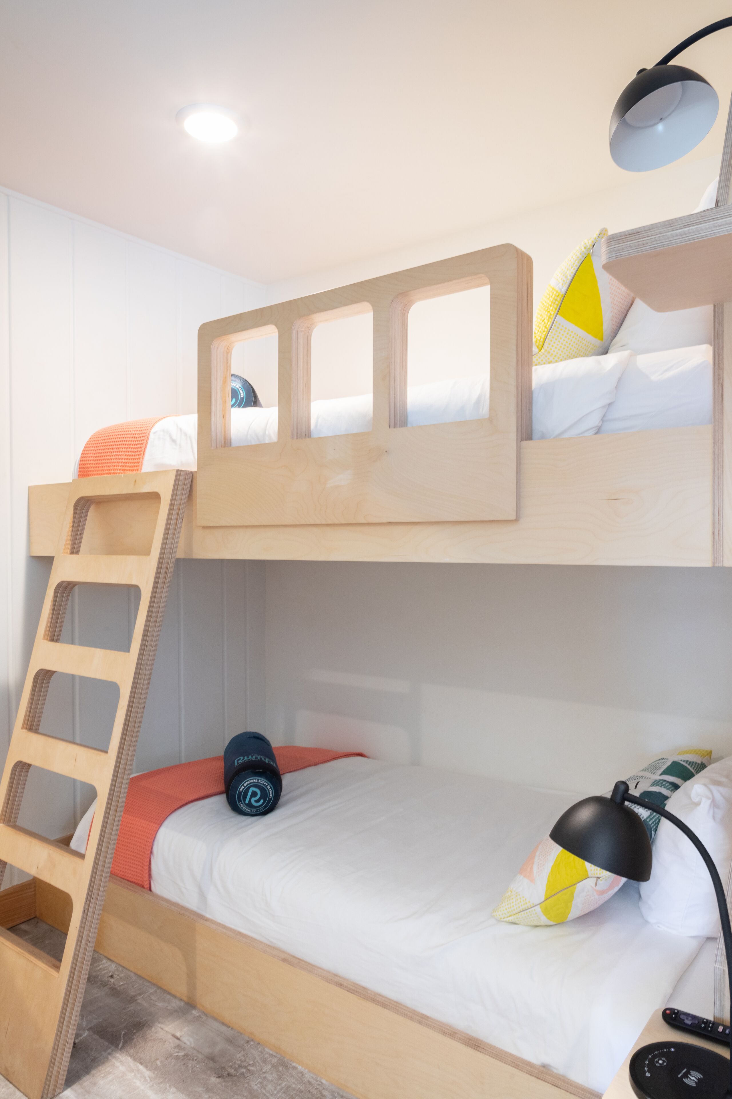 A bunk bed with a wooden ladder, a desk with a lamp, and a remote control on the side.