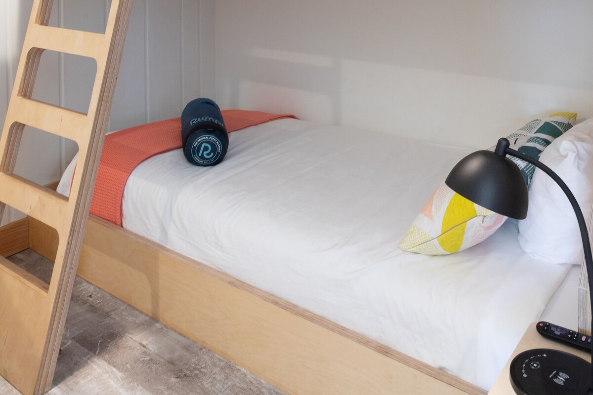 Ein Stockbett mit Holzlade, ein Schreibtisch mit Lampe und einer Fernbedienung daneben.