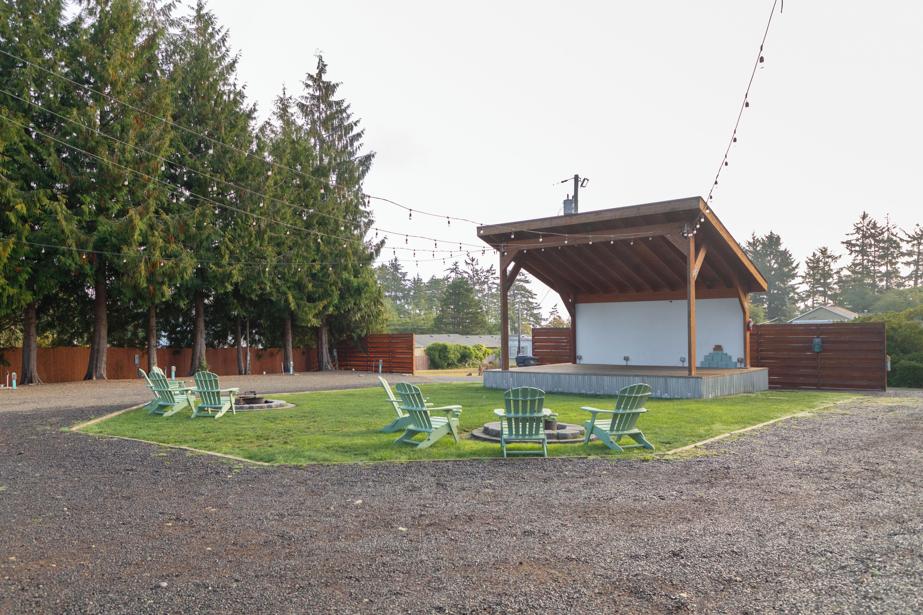 Un espace extérieur aménagé, partiellement abrité, avec des chaises et un foyer, entouré d’une zone recouverte de gravier et d’arbres.