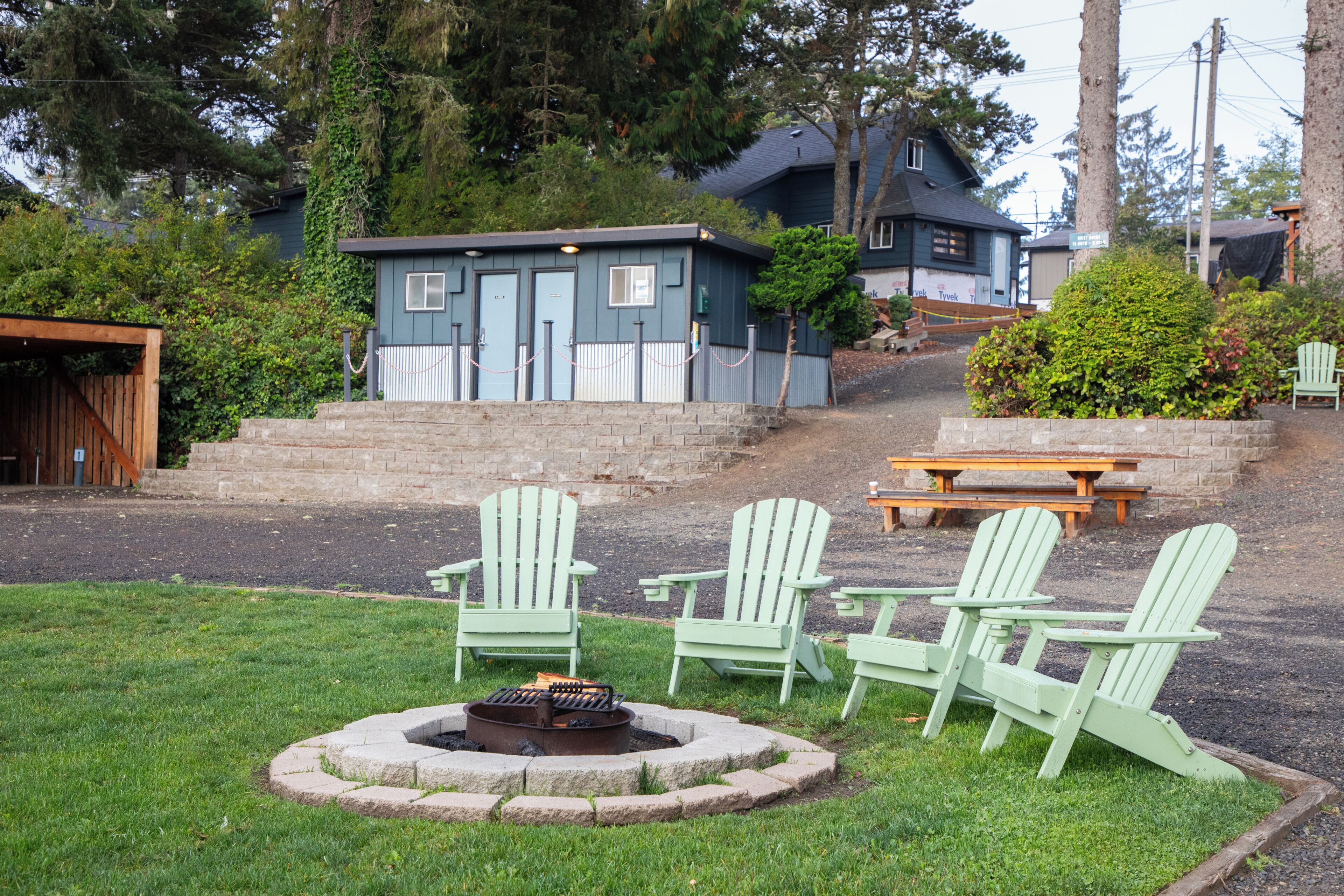 Une petite cabane avec un foyer, des chaises Adirondack vertes et une table de pique-nique.