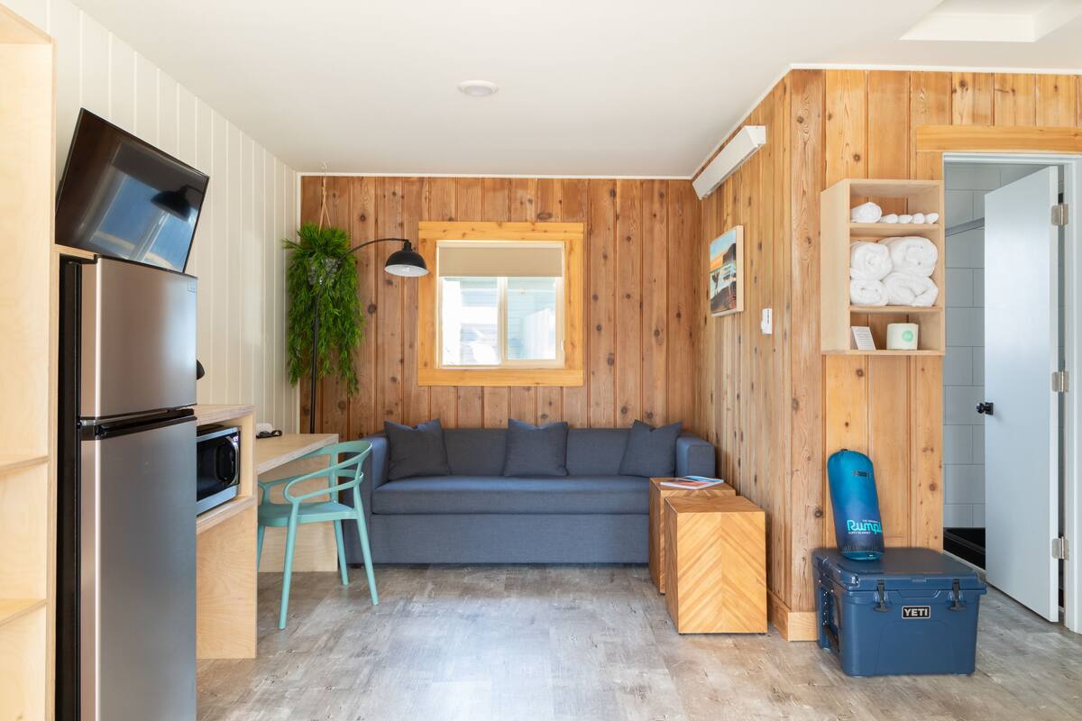 A compact living space with a kitchenette, a sofa, a small table, and a blue storage box.