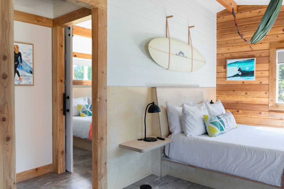 A bedroom with a bed, a nightstand, a surfboard, and a hammock.