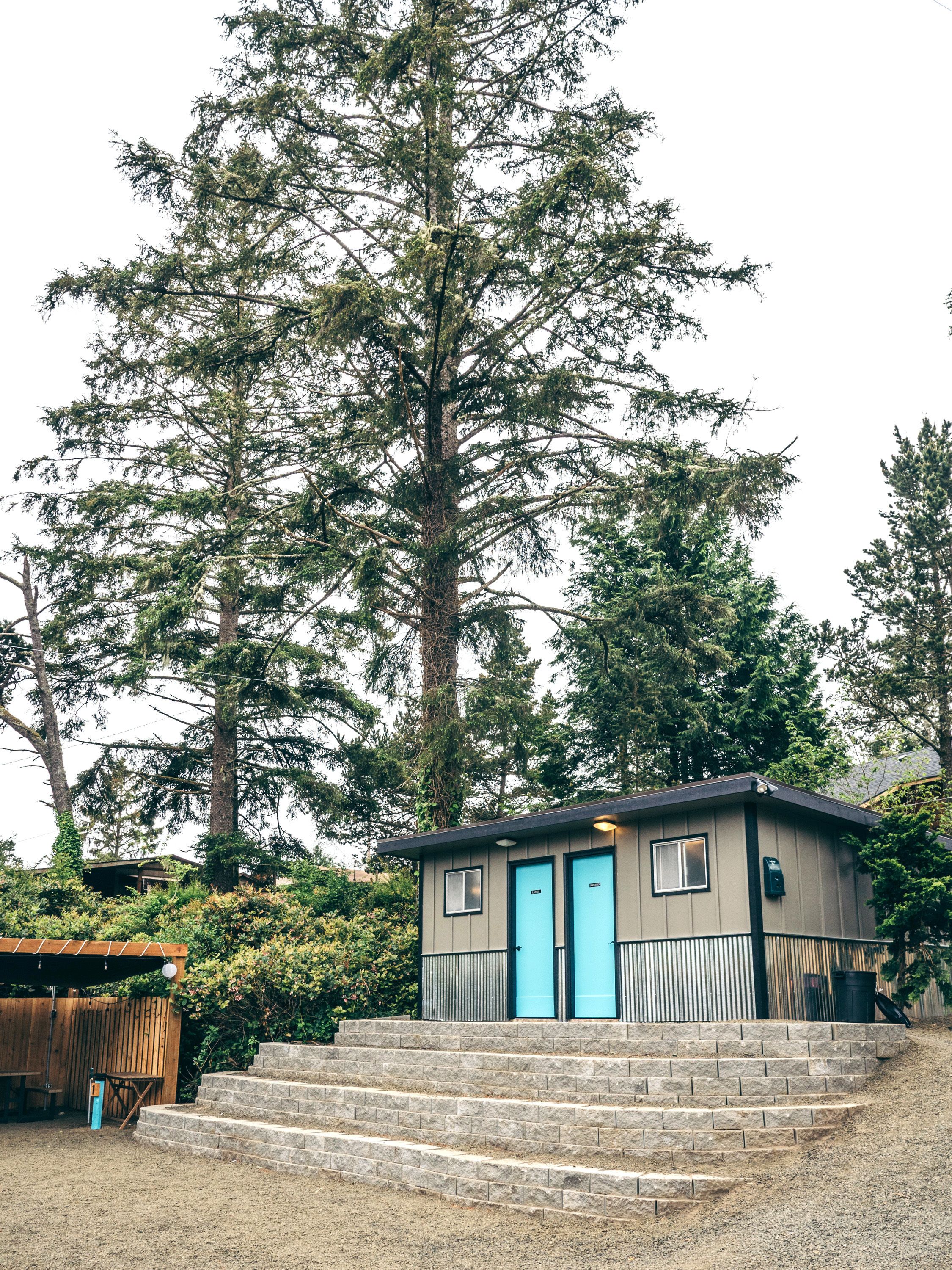 A small cabin with two blue doors, a wooden deck, and a staircase leading up to it.