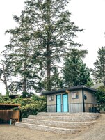 Una cabaña pequeña con dos puertas azules, una terraza de madera y una escalera que lleva a ella.