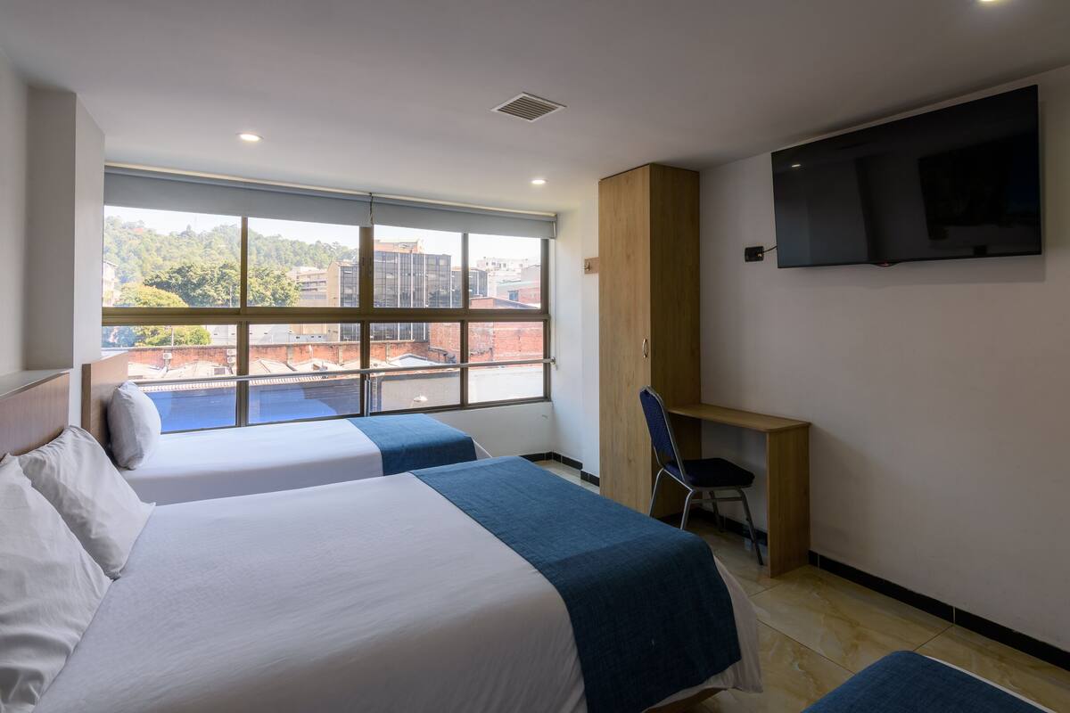 Hotelkamer met twee bedden, een bureau, een stoel, een televisie en een groot raam met uitzicht op de stad.