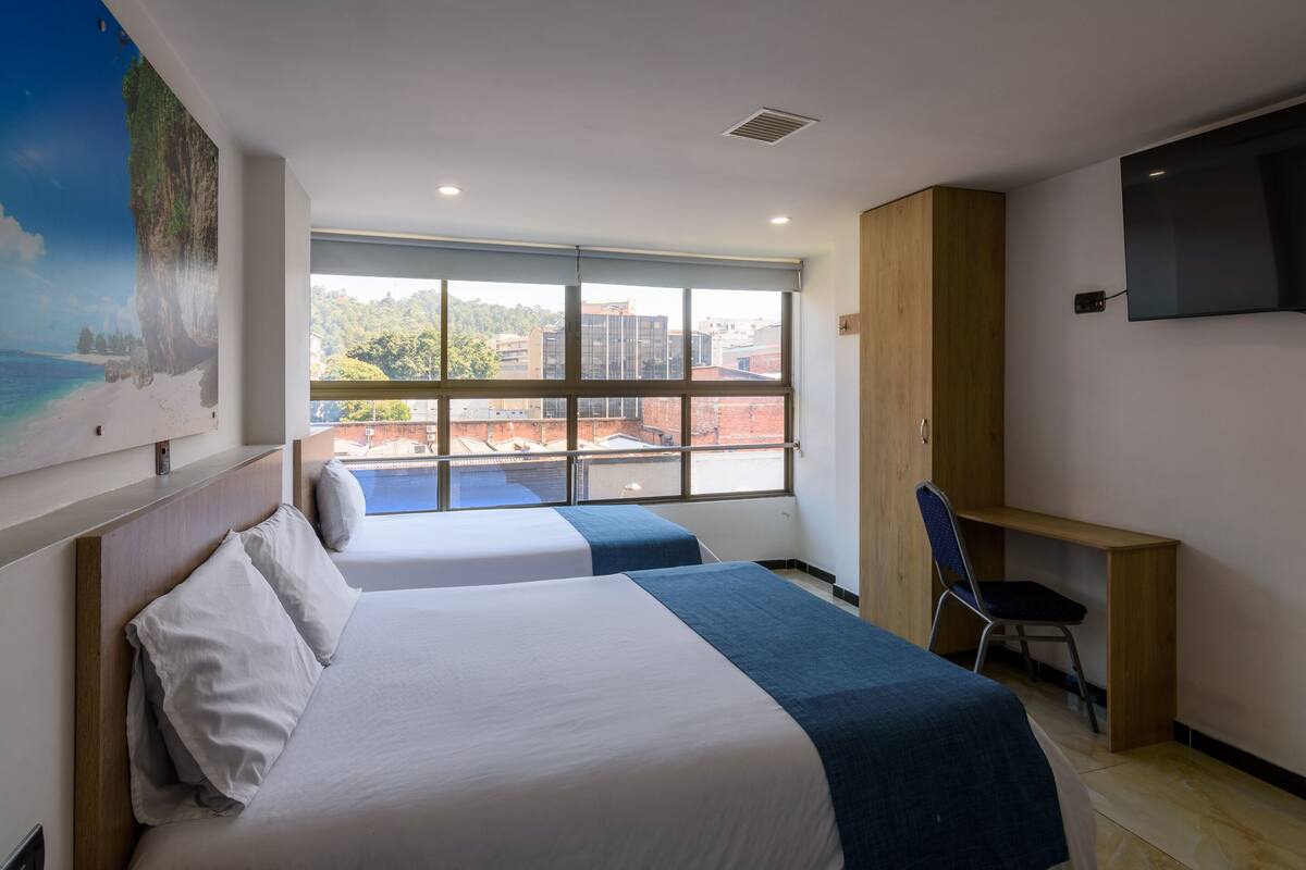 Hotelkamer met twee bedden, een bureau, een stoel, een televisie en een groot raam met uitzicht op de stad.