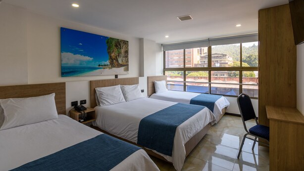 A hotel room with two beds, a desk, a chair, and a large window with a city view. - Hotel Med Estadio (Medellín)