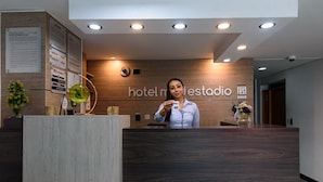 A hotel reception desk with a wooden finish, a digital screen, and a sign reading "hotel mdestradio". - Hotel Med Estadio (Medellín)