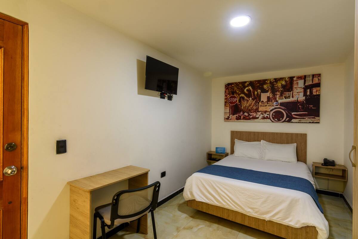 Een hotelkamer met een bed, bureau, stoel, televisie en een poster aan de muur.