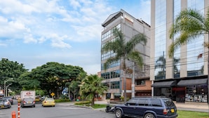 A hotel with a modern glass facade, a visible entrance, and a parking area with cars. - Hotel Med Estadio (Medellín)