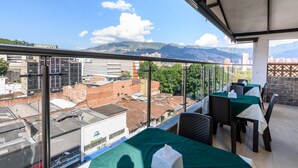 A rooftop terrace with tables and chairs, offering a view of a cityscape and mountains. - Hotel Med Estadio (Medellín)