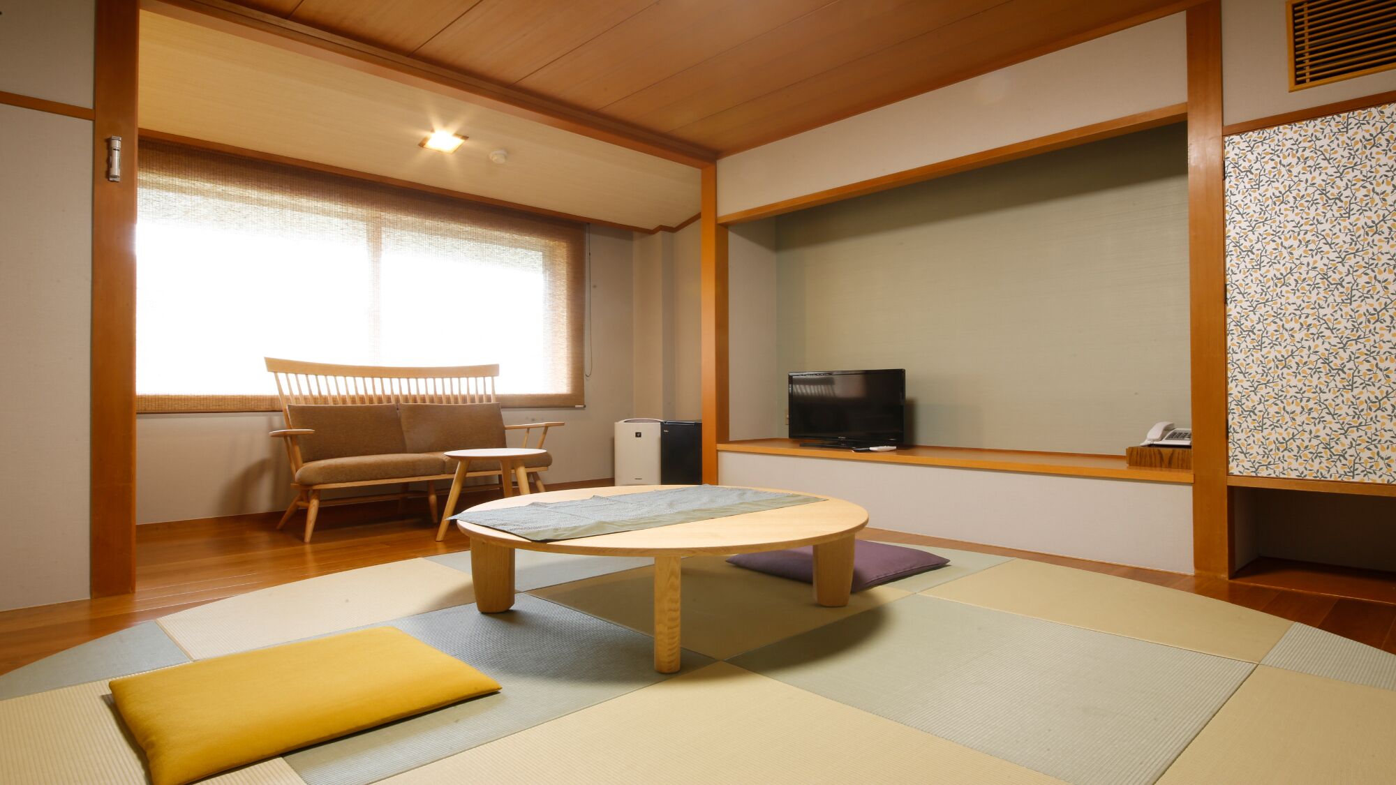 Et traditionelt japansk rum med tatamimåtter, et lavt bord, en sofa, et fjernsyn og en tapetvæg.