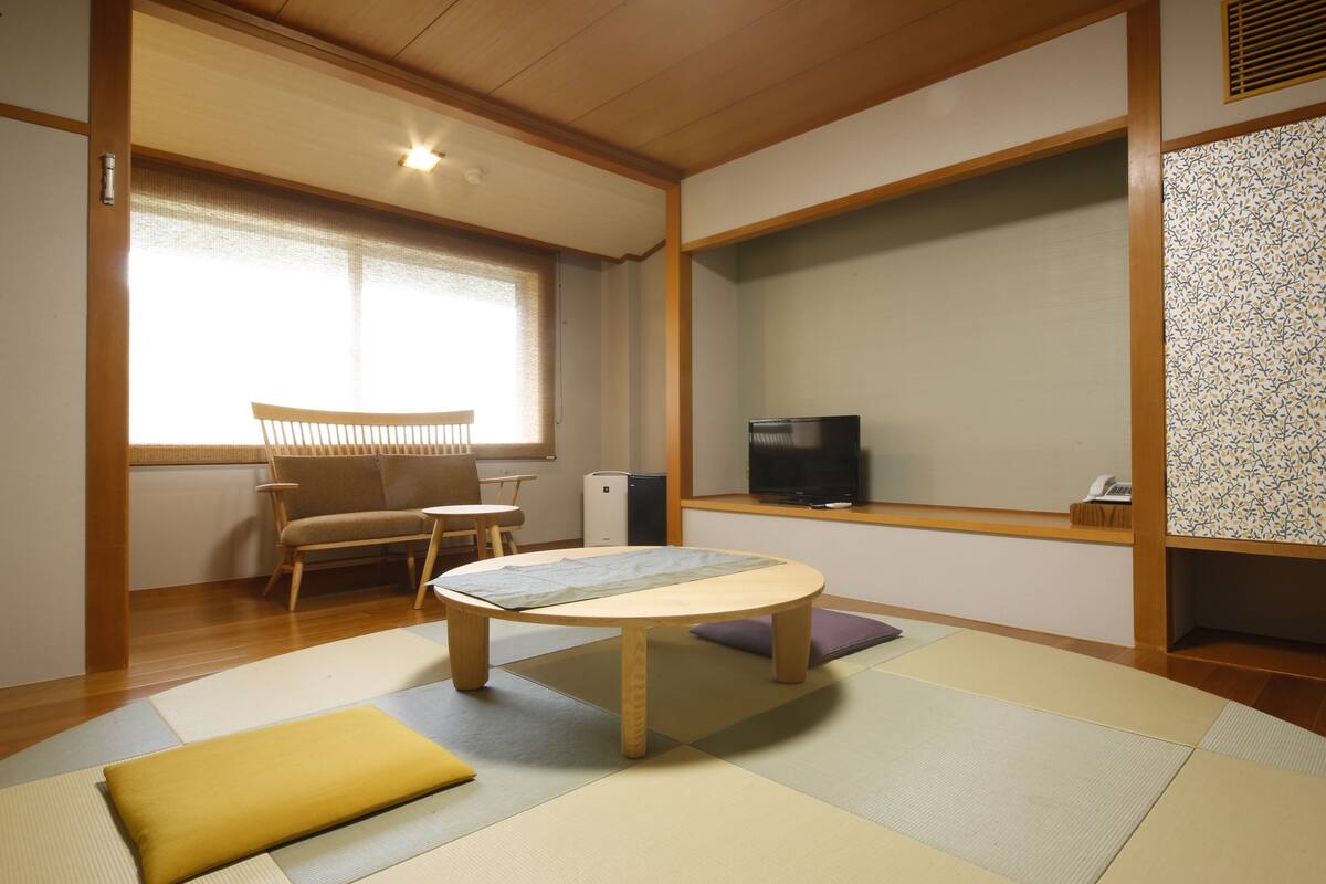 A traditional Japanese-style room with tatami flooring, a low wooden table, a sofa, and a television on a shelf.