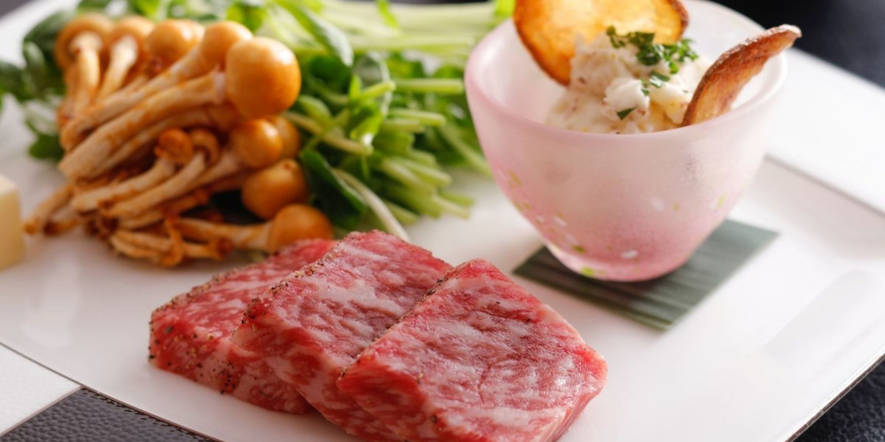 A plate with sliced meat, mushrooms, and greens, and a bowl of sauce.