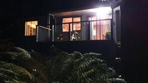 A modern house with large windows and a balcony, surrounded by dense foliage.
