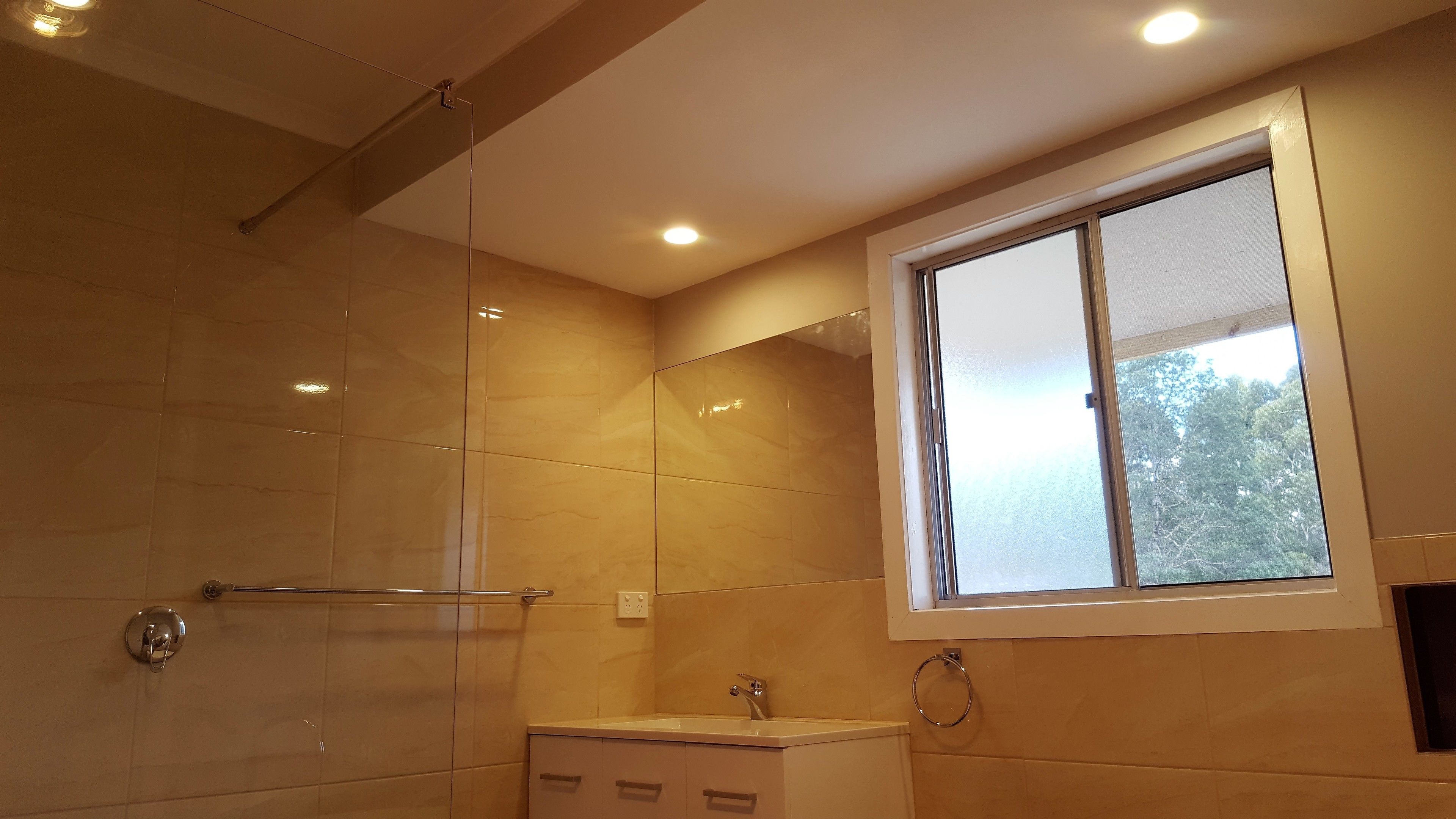 A modern bathroom with a glass shower enclosure, a sink with a mirror, and a window providing natural light.