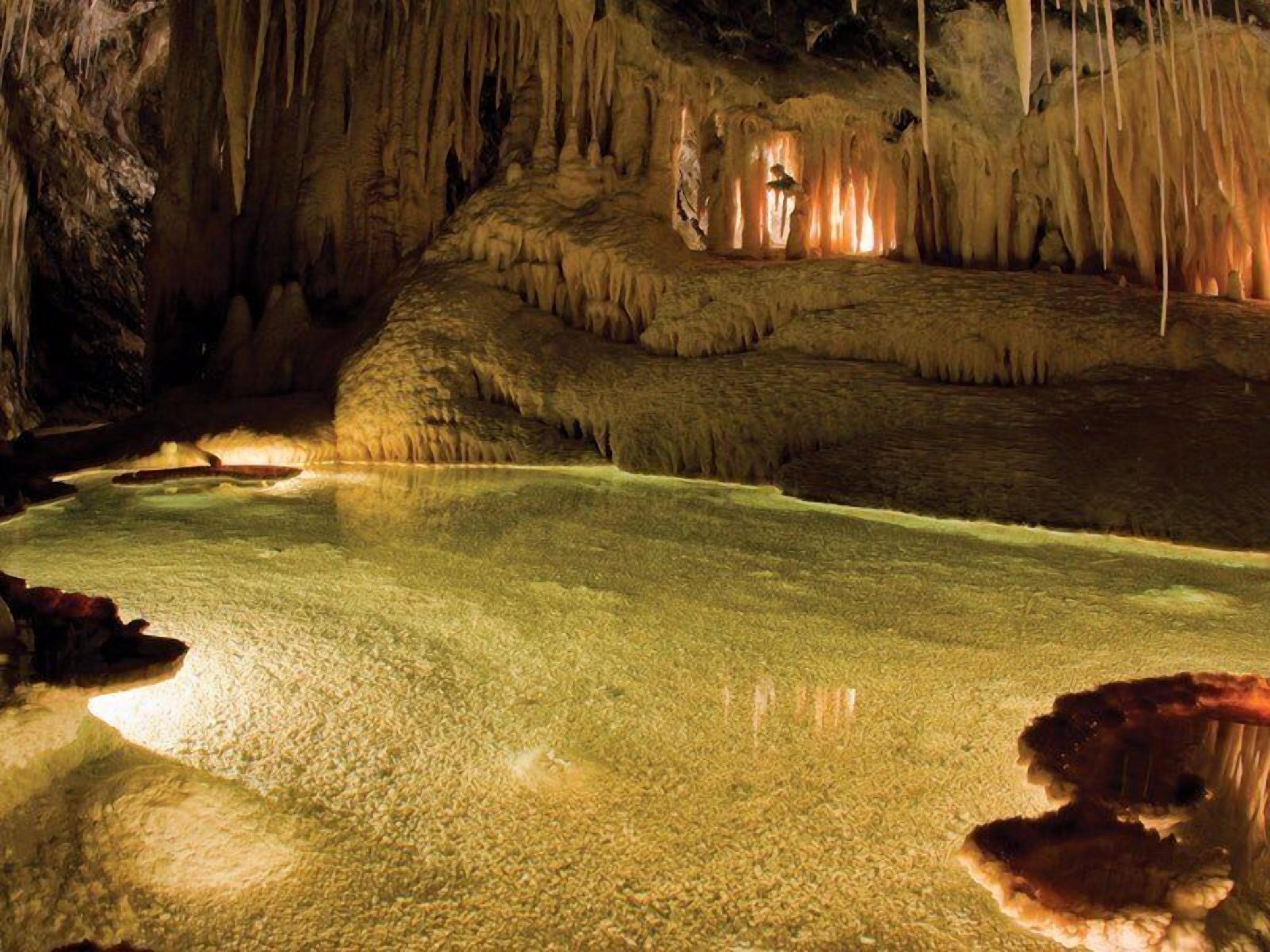 Een grot met stalactieten en -stalagmieten, een reflecterend wateroppervlak en een grotbodem.