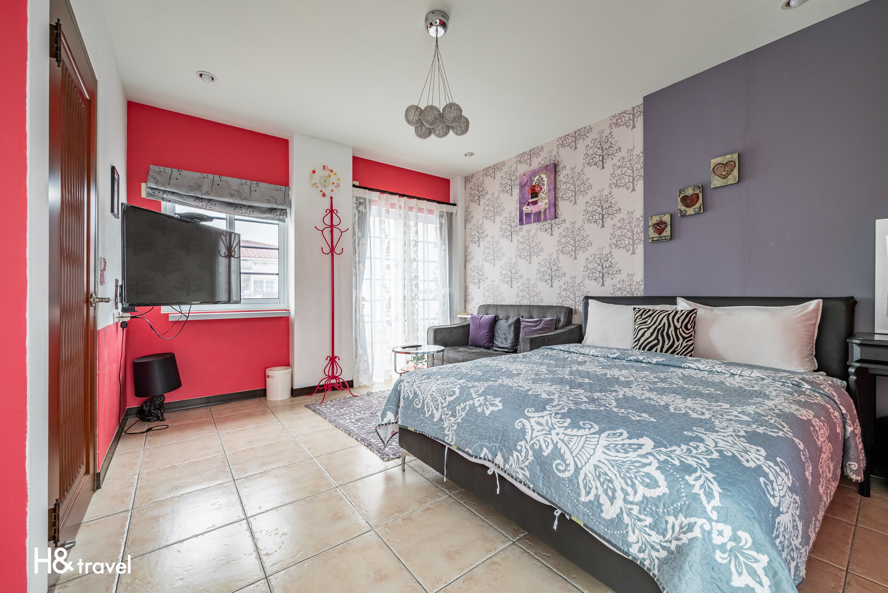 A bedroom with a large bed, a TV, a window with curtains, and a red wall.