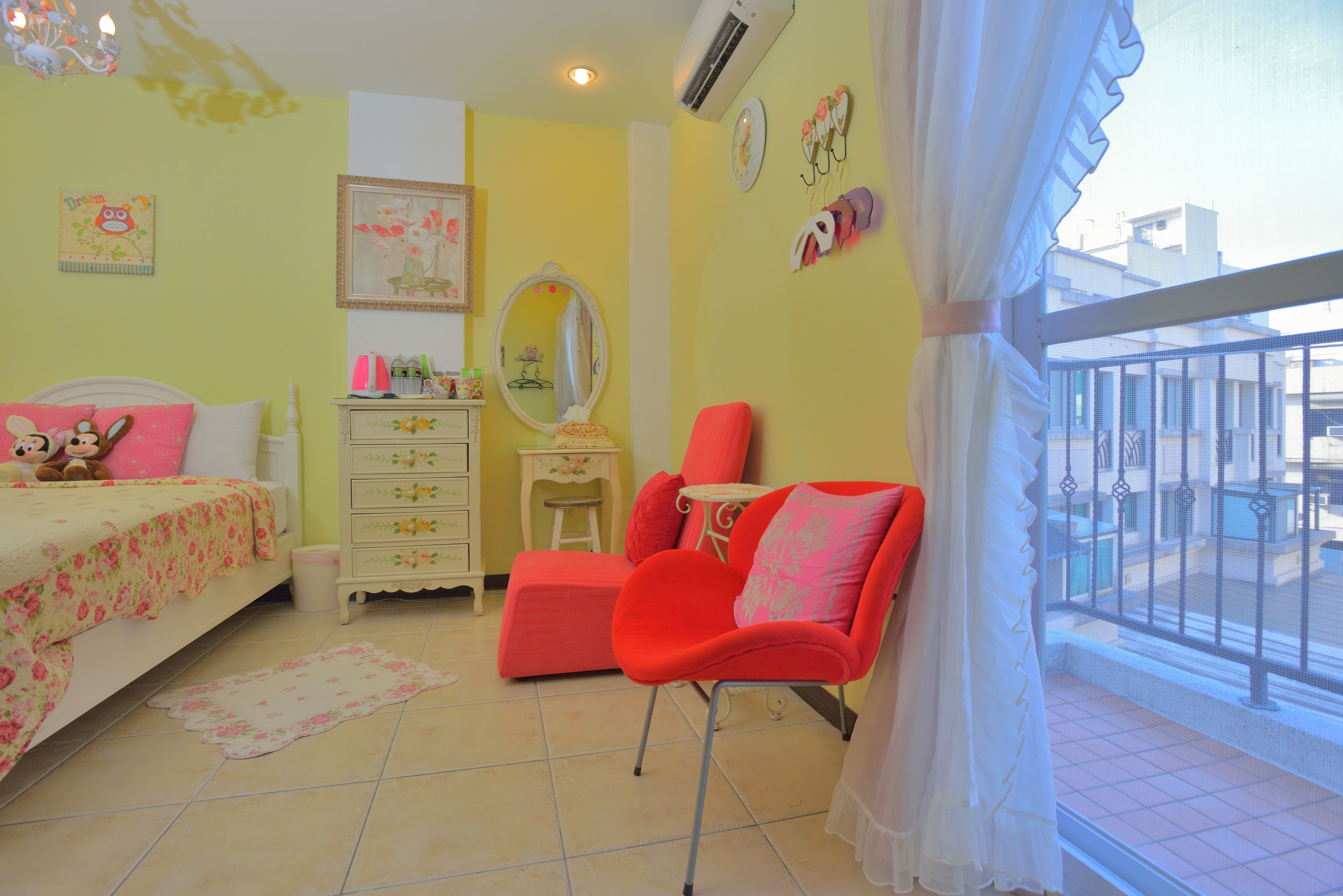 A bedroom with a bed, a dresser, a chair, a mirror, and a window with a balcony view.