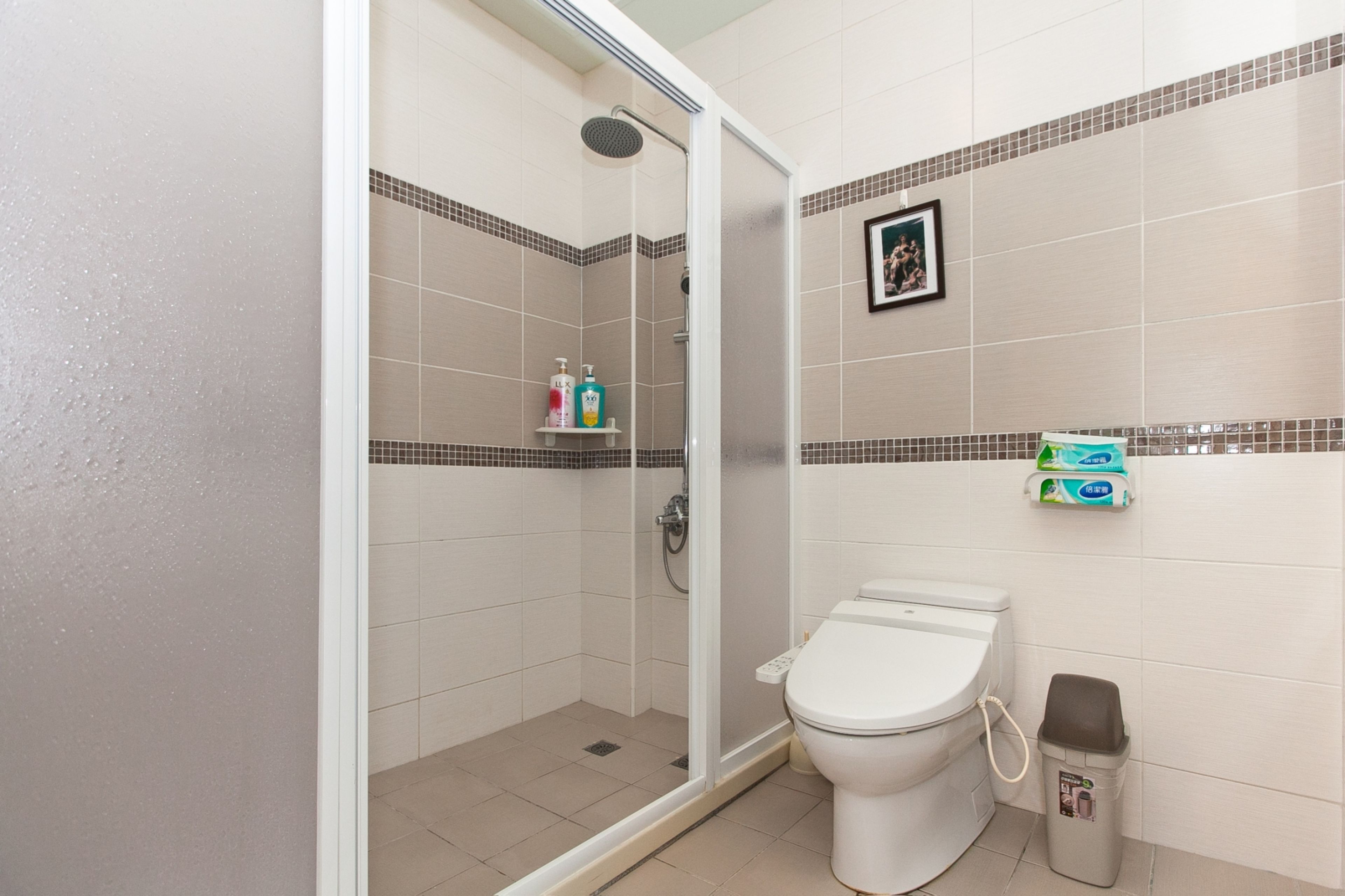A bathroom with a shower, toilet, and a trash bin.
