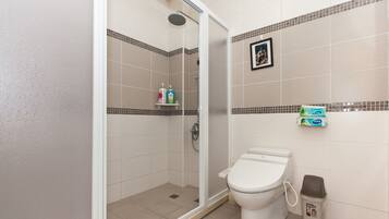 A bathroom with a shower, toilet, and a trash bin.