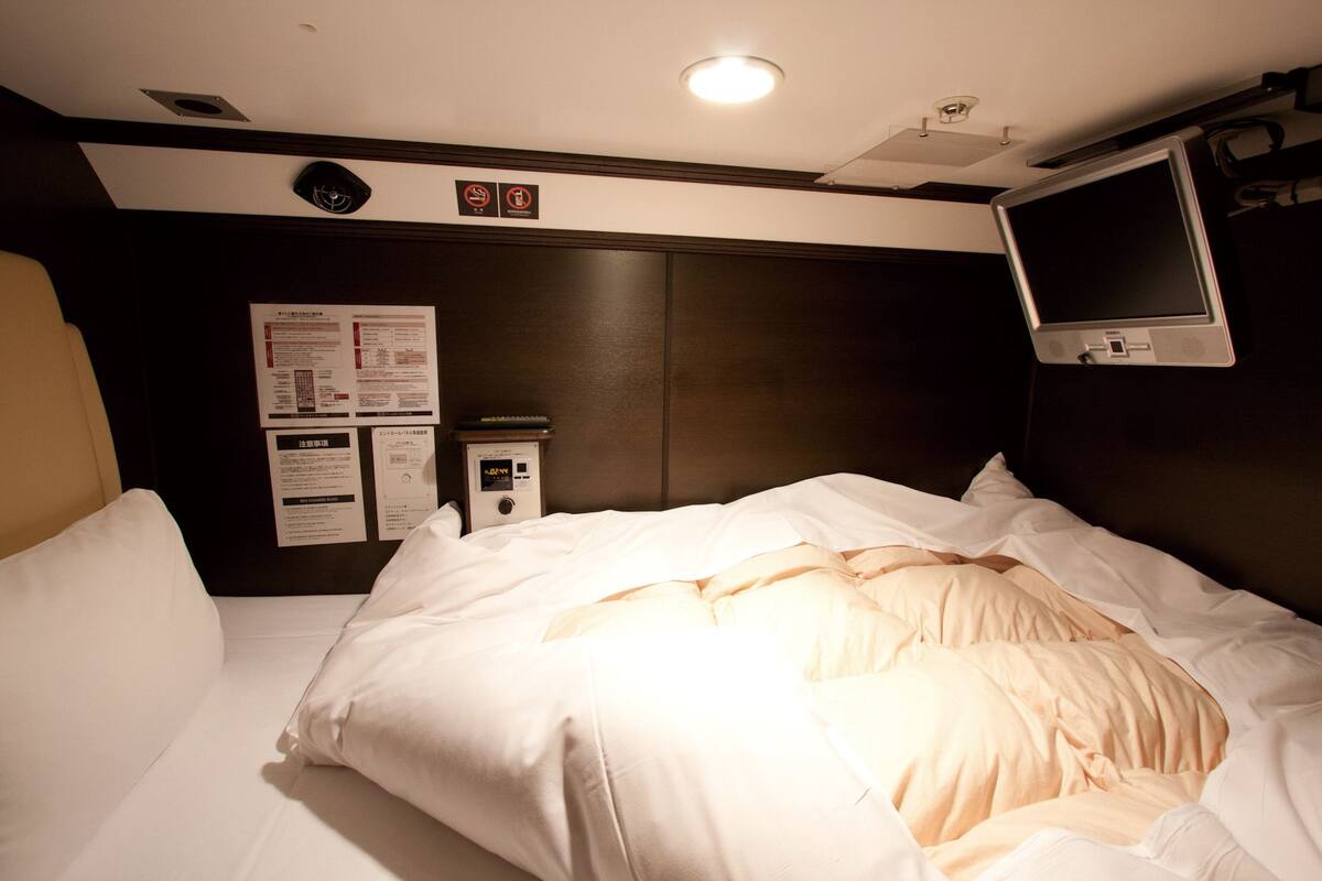 A hotel room with a bed, a TV mounted on the wall, and a control panel on the wall.