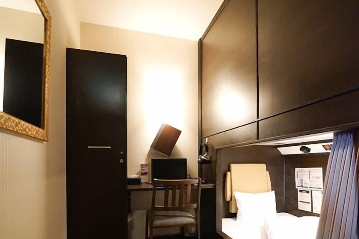 A compact hotel room with a bed, a desk, a chair, a mirror, and a wardrobe.