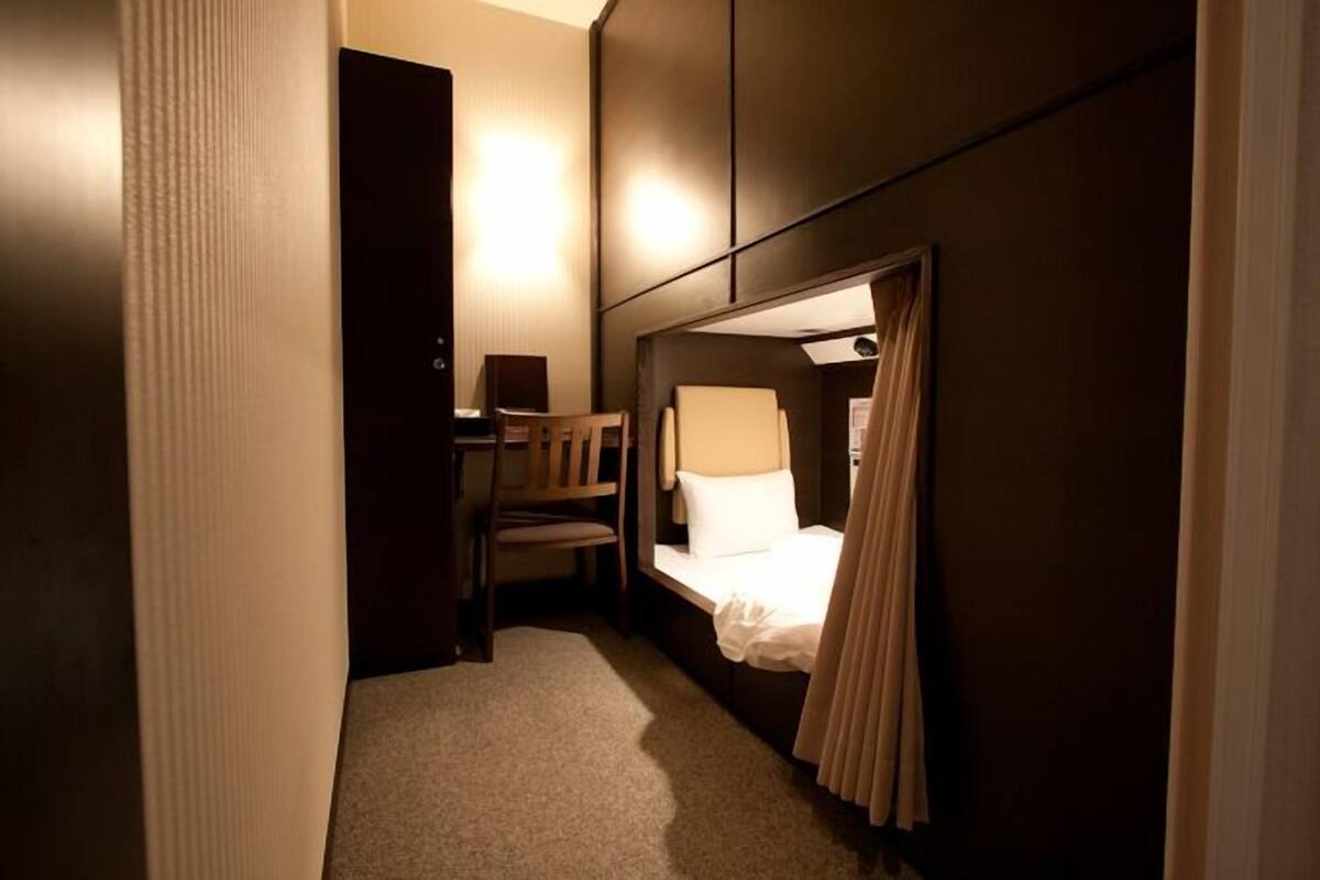 A compact hotel room with a single bed, a chair, a desk, and a wall-mounted cabinet.