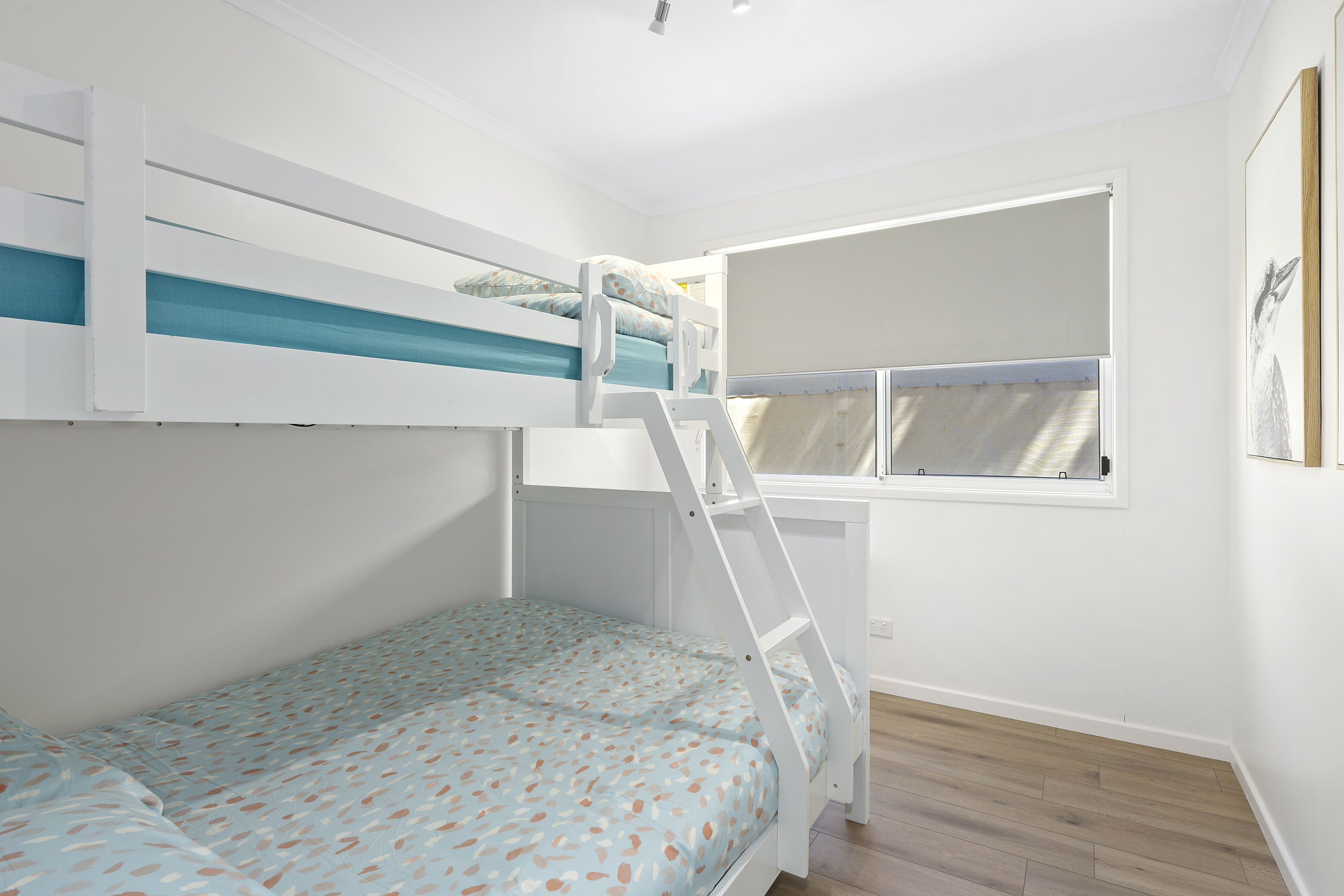 A room with a bunk bed, a window with curtains, and a wooden floor.