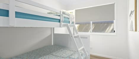 A room with a bunk bed, a window with curtains, and a wooden floor.
