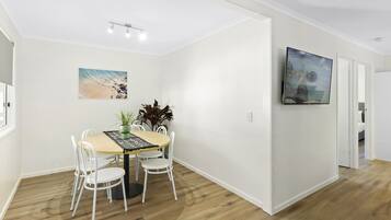 A dining area with a table and chairs, a plant, and a painting on the wall.