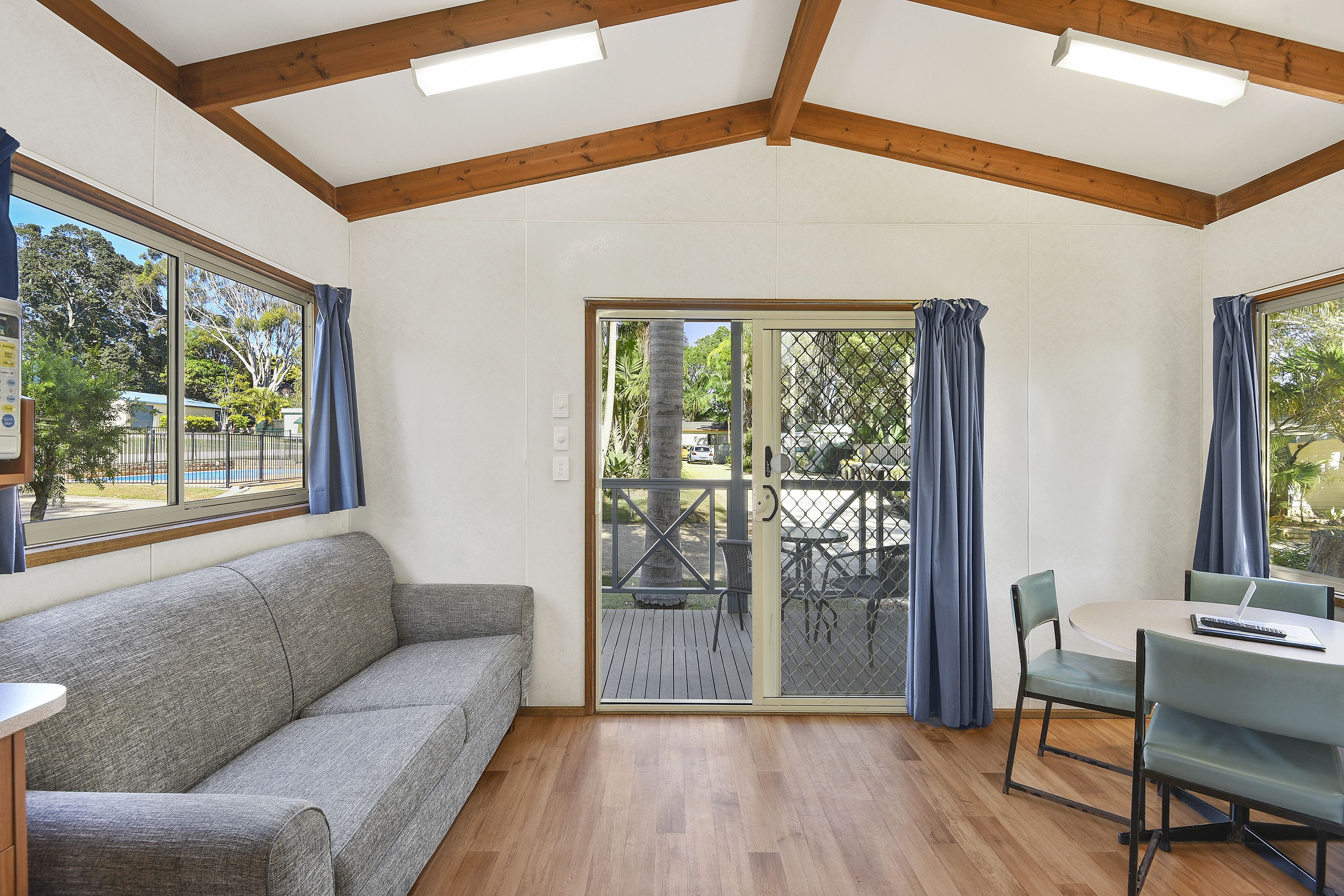 A room with a grey sofa, a table with chairs, and a sliding glass door leading to an outdoor area.