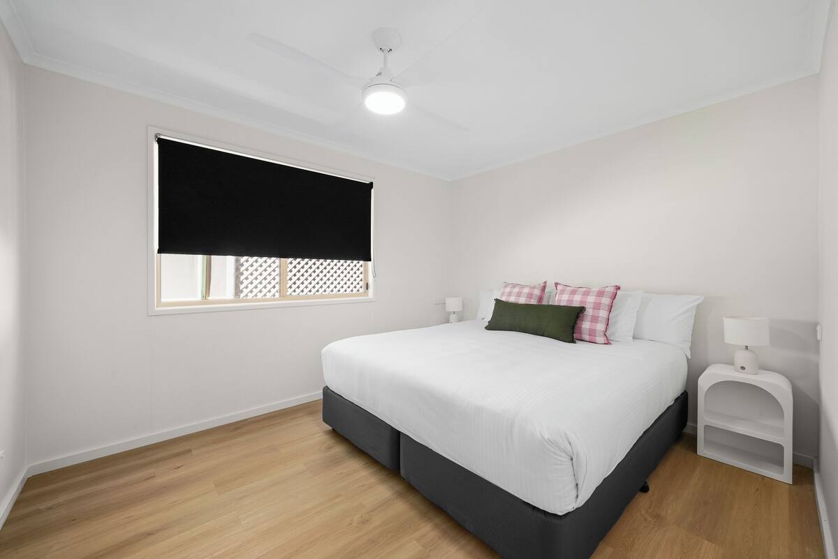 A bedroom with a bed, a nightstand, a lamp, a window with a blind, and a ceiling fan.