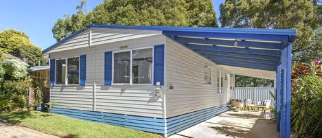 A single-story mobile home with a covered porch, a small garden, and a clear blue sky.