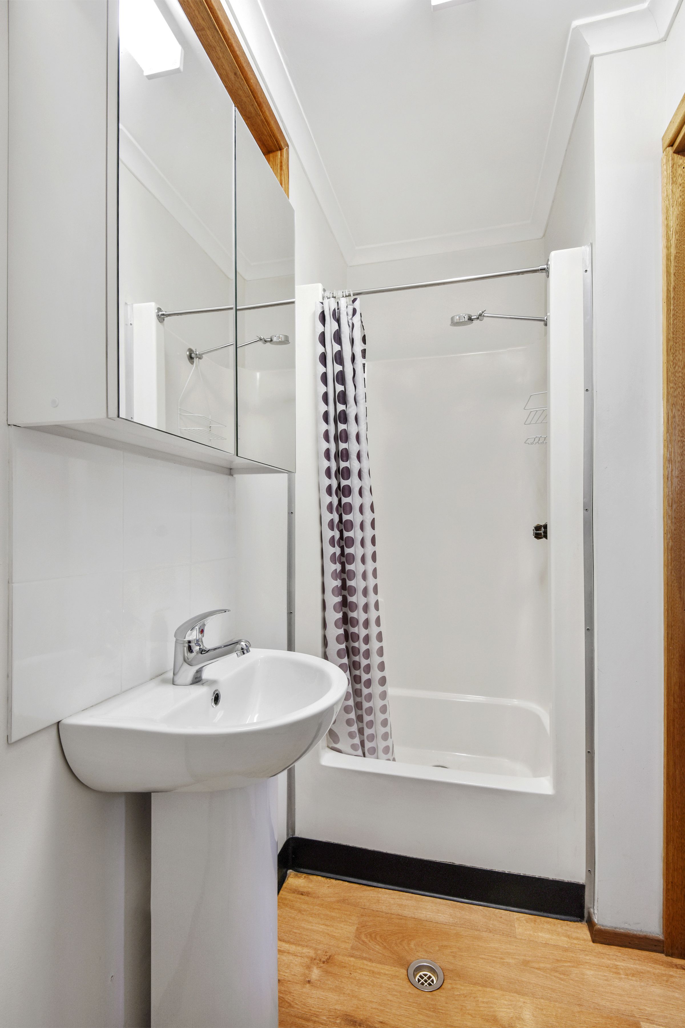 Un baño moderno con lavamanos, espejo y ducha blancos.