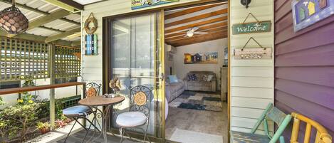 A beach house with a sliding glass door, a small patio with a table and chairs, and a 'Welcome' sign.