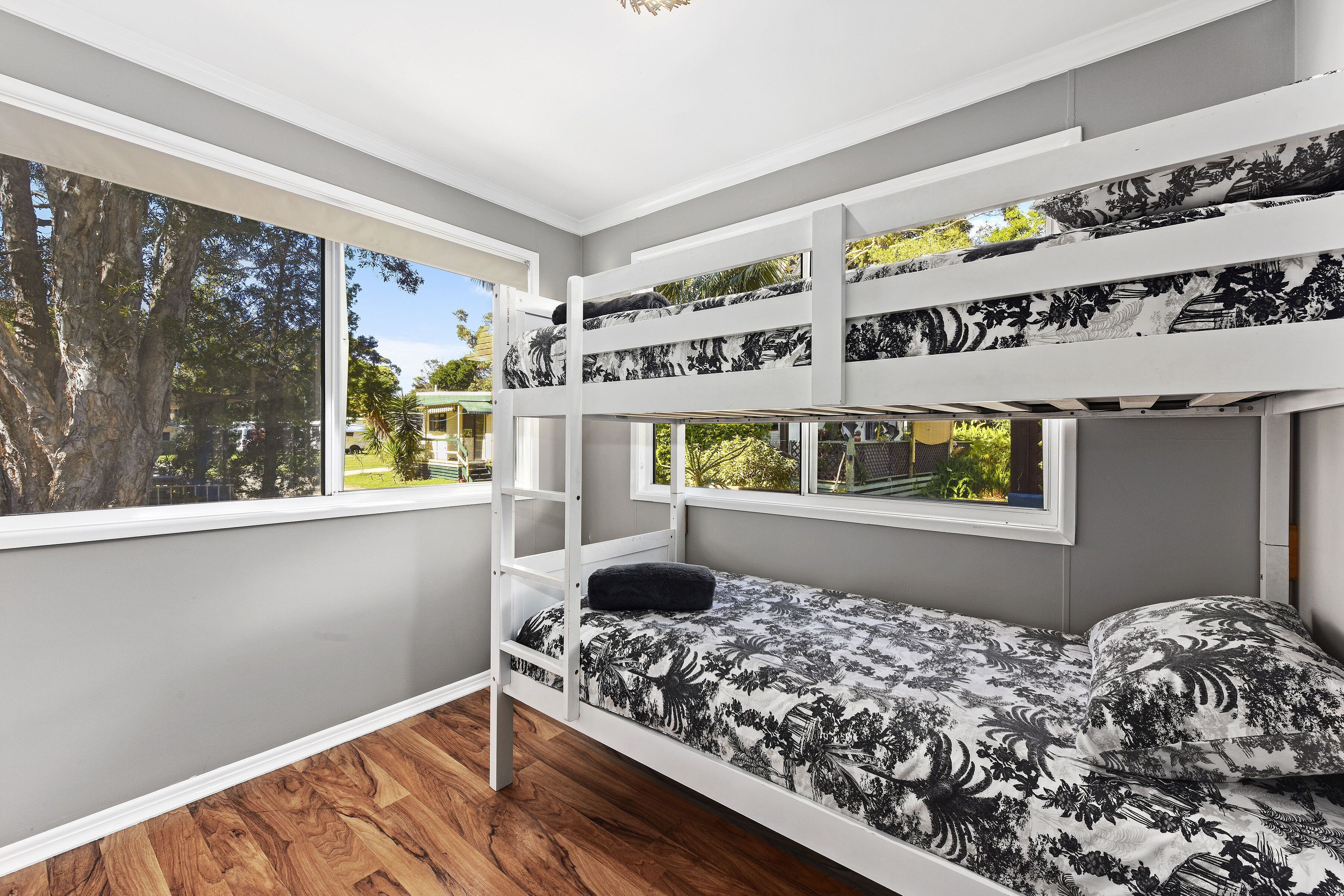 Une chambre avec des lits superposés, donnant sur des arbres et un bâtiment à l’extérieur.
