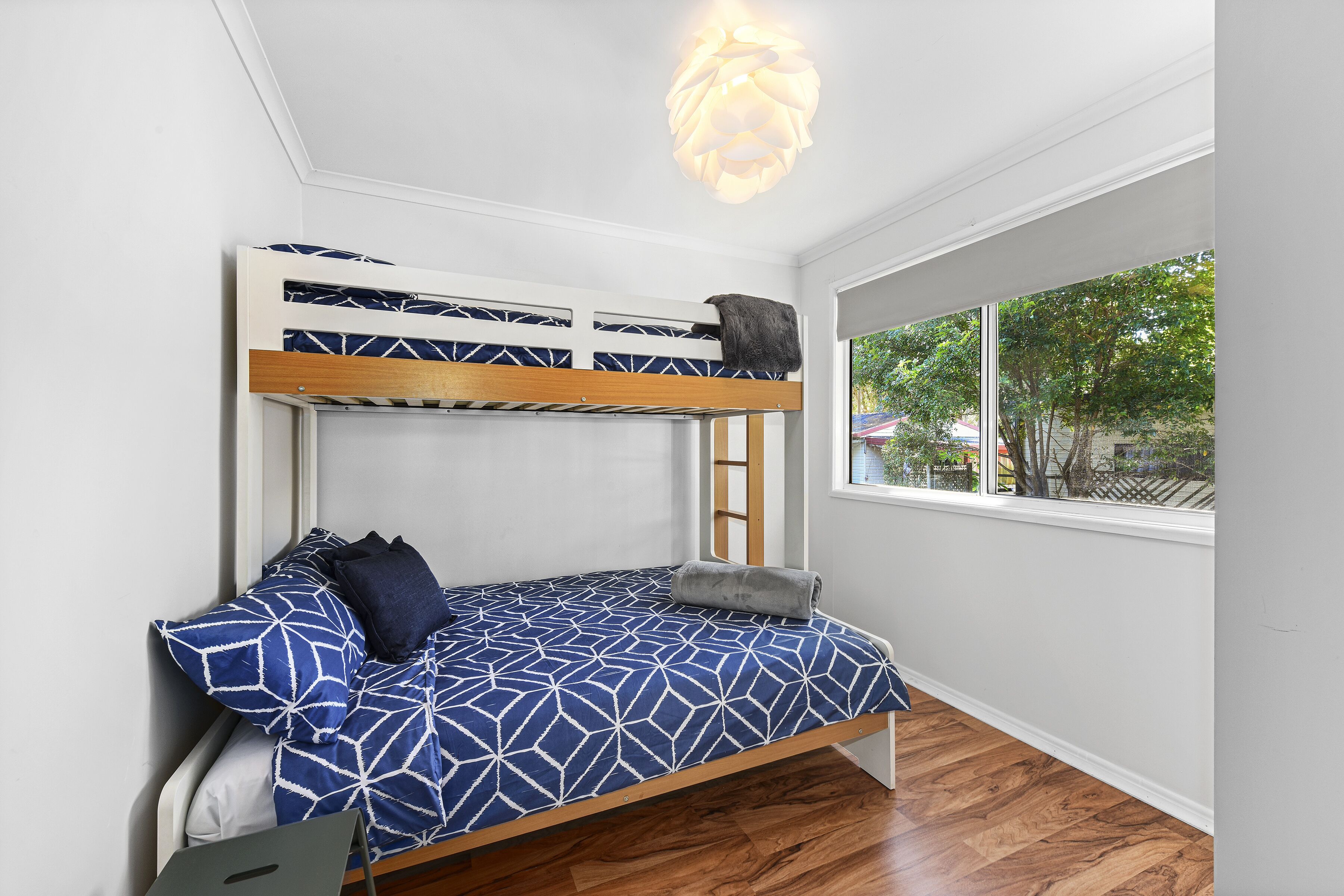 A bunk bed with a geometric-patterned bedspread, a wooden headboard, and a window with a view of trees and buildings.