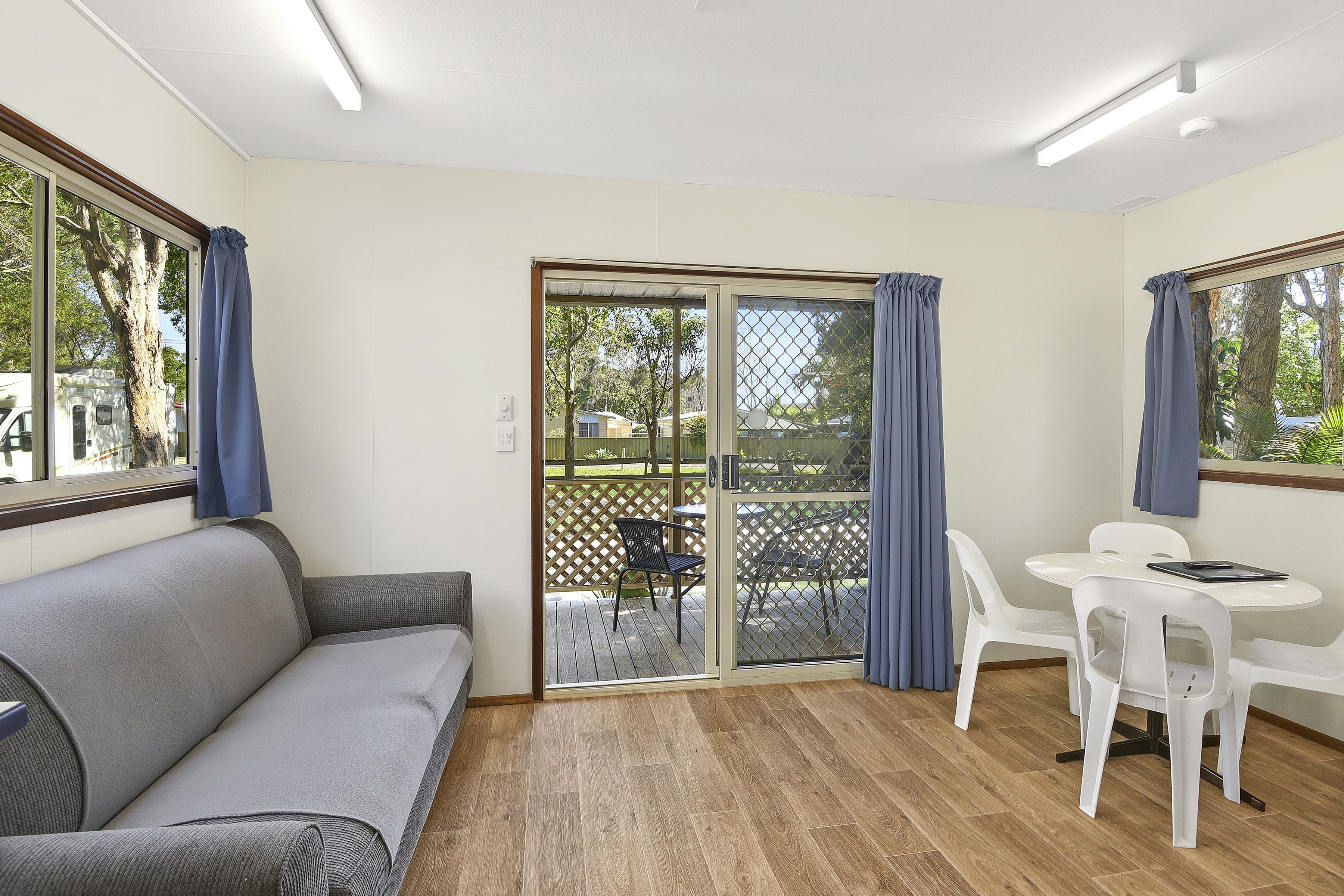 A room with a sofa, a table with chairs, and a sliding glass door leading to an outdoor area with a wooden deck.