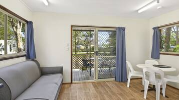 A room with a sofa, a table with chairs, and a sliding glass door leading to an outdoor area with a wooden deck.