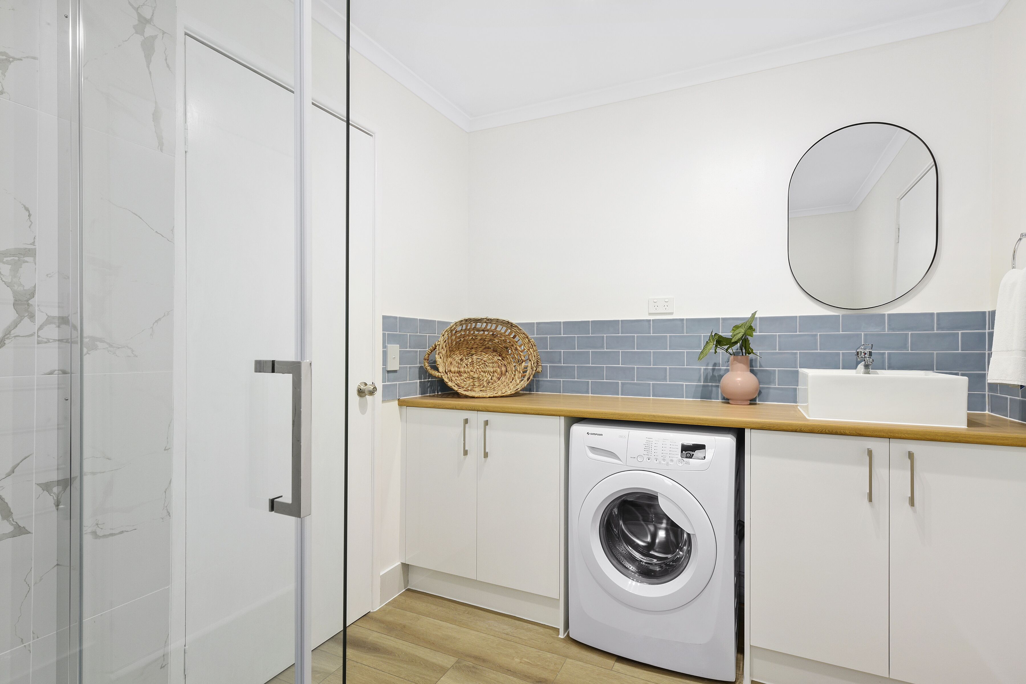 Een kleine wasruimte met een wasmachine, een wasbak en een spiegel.