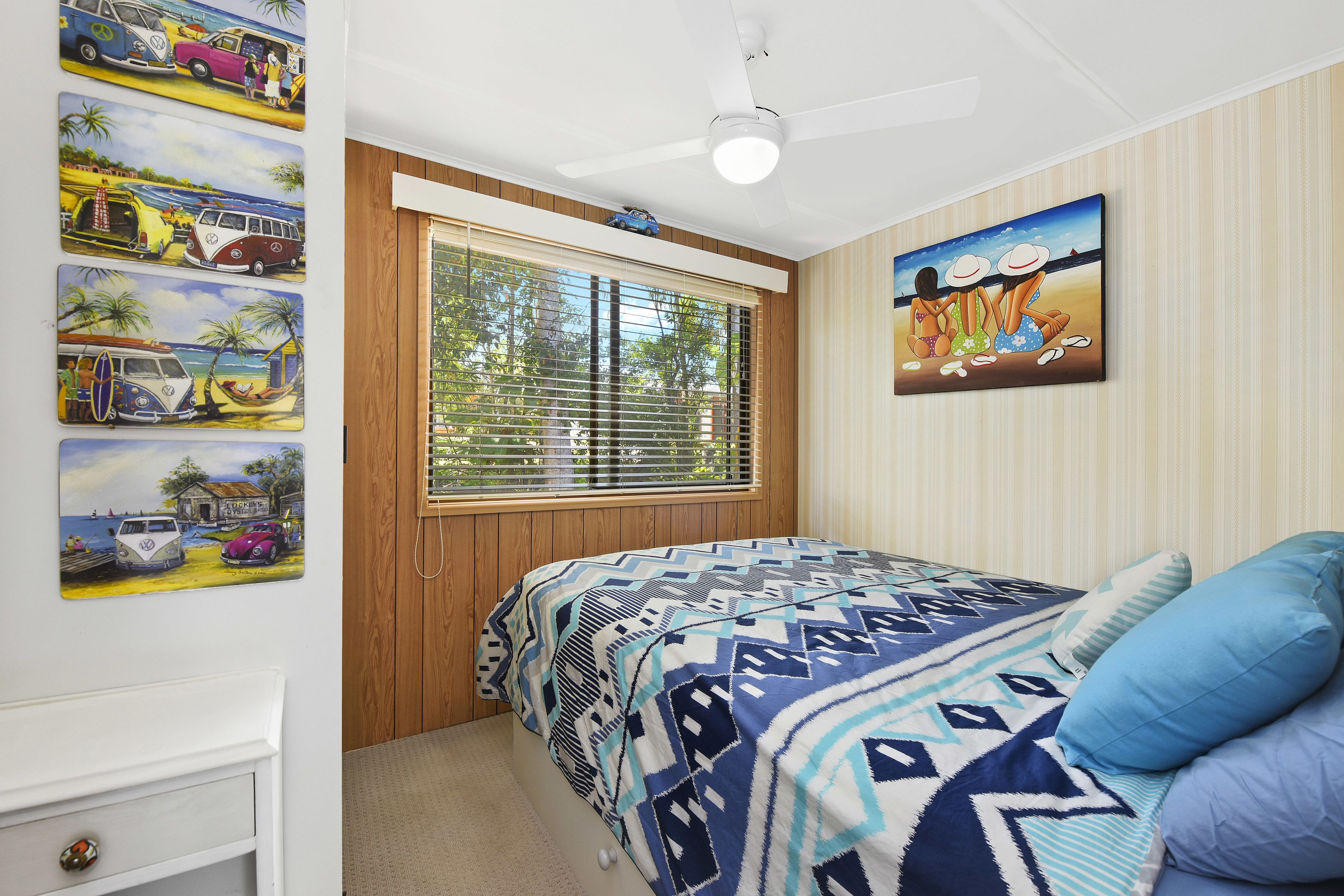 A bedroom with a bed, a window with blinds, a ceiling fan, and wall art.