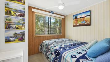 A bedroom with a bed, a window with blinds, a ceiling fan, and wall art.