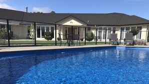 A swimming pool with clear blue water, surrounded by a covered patio area with outdoor seating. - Grasslands Bed & Breakfast (Cambridge)