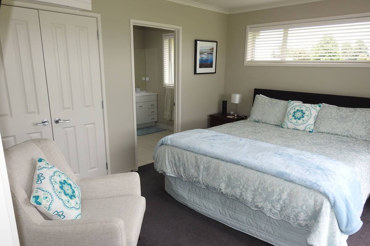 A bedroom with a bed, a chair, a wardrobe, a bathroom, and a window.