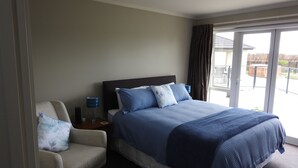 A hotel room with a bed, a chair, a nightstand, and a view of the outside. - Grasslands Bed & Breakfast (Cambridge)
