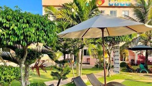 Un resort con mesas al aire libre, palmeras y un edificio con un cartel al fondo.