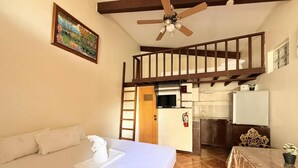 Un dormitorio con cama, ventilador de techo, un cuadro, kitchenette y una escalera.
