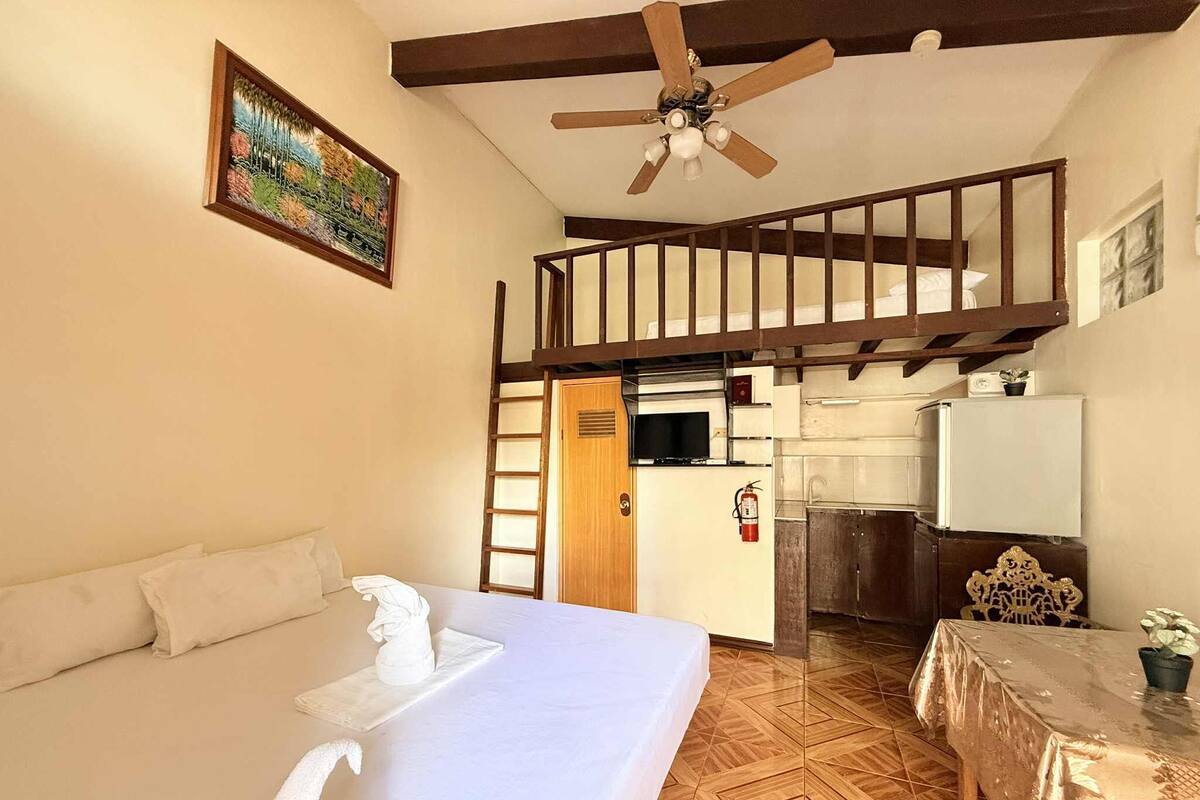 Une chambre à coucher comprenant un lit, un ventilateur de plafond, un tableau, un coin cuisine et un escalier.