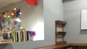 Una zona de bar con una barra larga y tres sillas de madera. Hay una estantería con libros y un jarrón con flores sobre la barra.